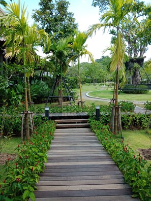 A wooden pathway leading through a lush garden with palm trees and red flowers.