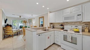 A modern kitchen with white cabinets, a microwave, an oven, and a yellow kettle.
