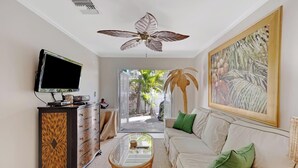 A living room with a flat-screen TV, a ceiling fan, a sofa, a coffee table, and a painting.