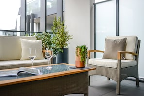 Ein moderner Außenbereich mit Sitzgelegenheit, einem Korbsessel, einem Glastisch mit einer Zeitschrift und einem Blumentopf.