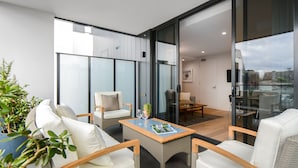 Ein modernes Wohnzimmer mit Rattanmöbeln, einer Glastür, die auf einen Balkon führt, und Blick auf die Stadtlandschaft.