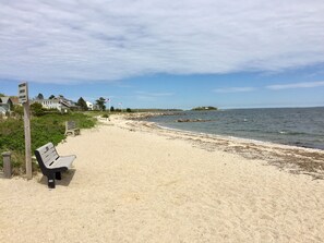 A sandy beach with a bench, a signpost, and a view of the ocean.
