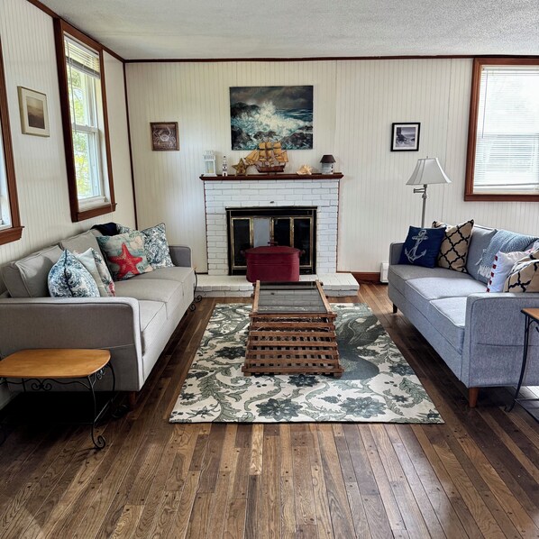 A living room with two sofas, a fireplace, wooden flooring, and a large window.