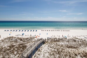 A beach with a wooden boardwalk leading to the shore, white sand, and a clear blue sky.