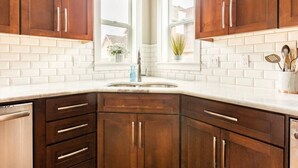 Una cocina con gabinetes de madera oscura, azulejos blancos tipo metro y un lavamanos de acero inoxidable.