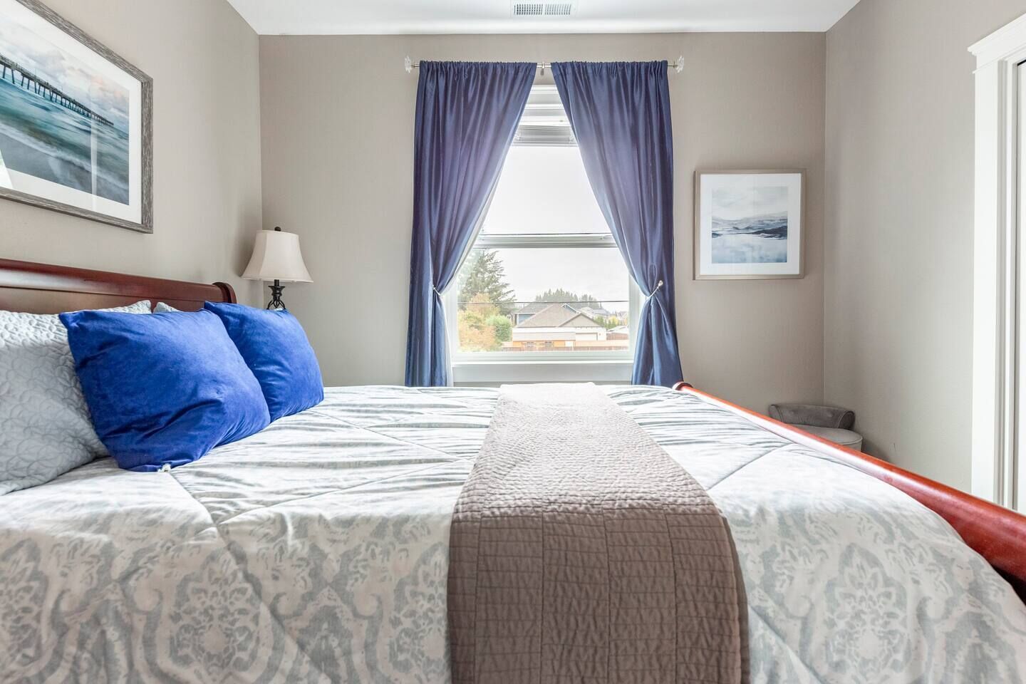 Une chambre d’hôtel avec un grand lit, deux oreillers, une table de chevet, une lampe et une fenêtre avec des rideaux.