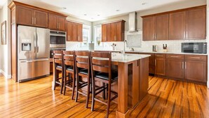 Una cocina moderna con armarios de madera, electrodomésticos de acero inoxidable y una isla central con taburetes de bar.