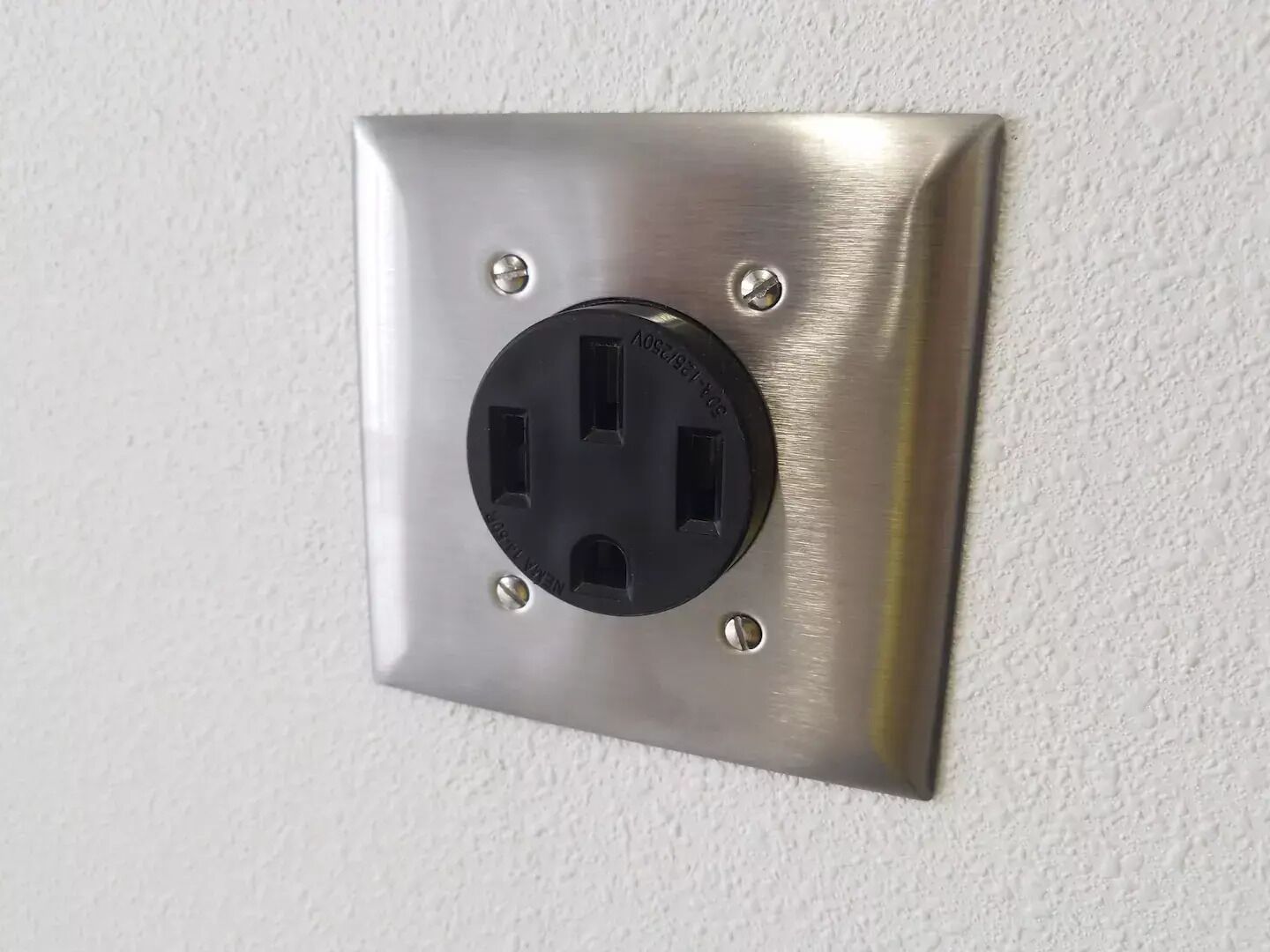 A wall-mounted electrical outlet with a metallic finish and four screws.