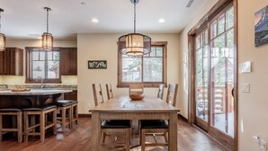 A spacious kitchen with a large dining table, wooden chairs, and pendant lighting. - Luxury Cabin with Private Hot Tub! Close to Village! (Mammoth Lakes)