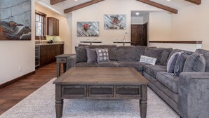 A spacious living room with a large sectional sofa, a wooden coffee table, and artwork on the walls. - Luxury Cabin with Private Hot Tub! Close to Village! (Mammoth Lakes)