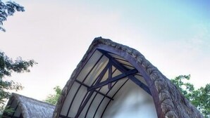 Une cabane à toit de chaume, dotée d’un balcon en bois et d’un escalier menant à l’entrée.
