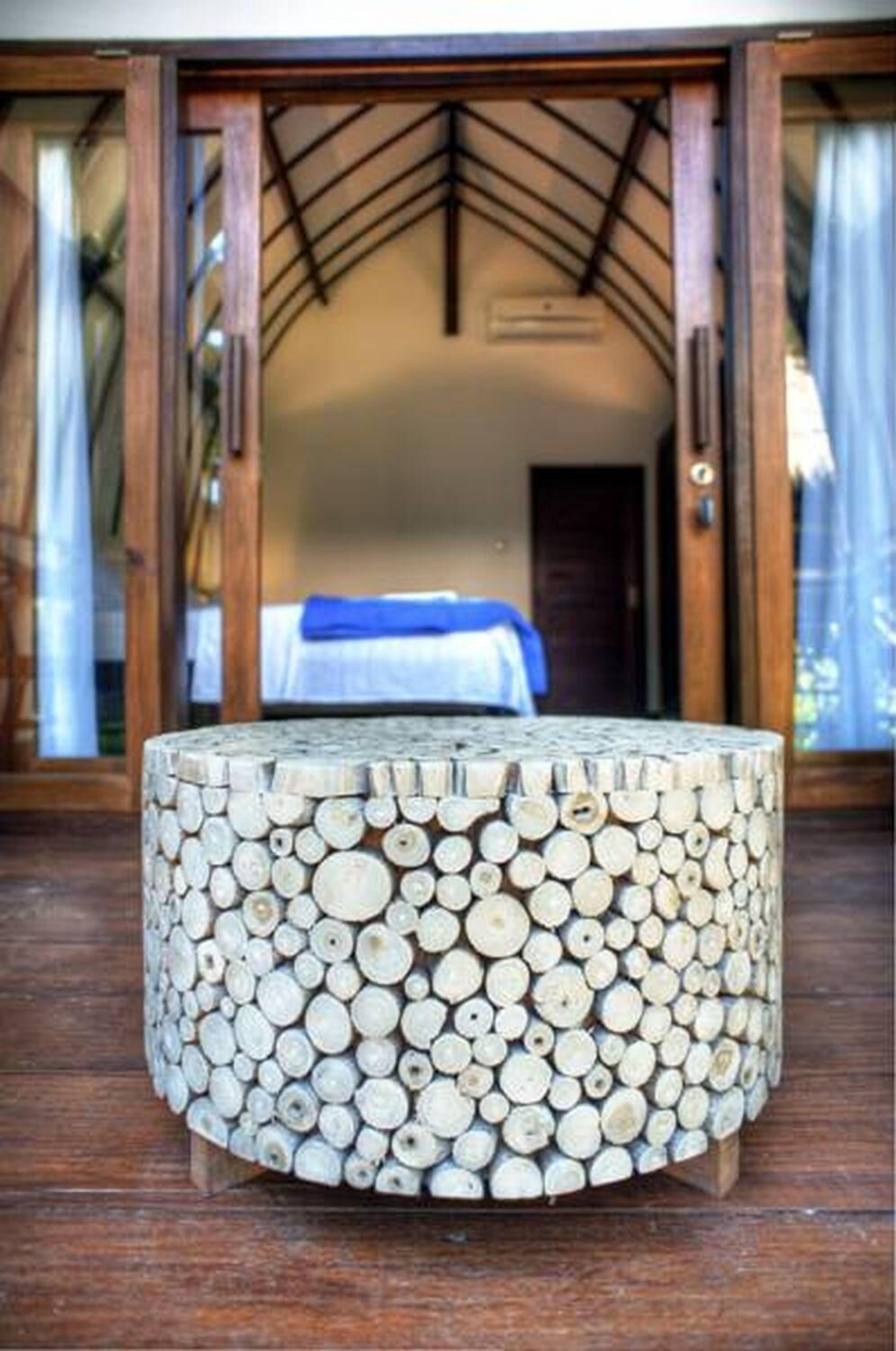 A round wooden table with a unique design made from stacked logs, placed on a wooden deck.