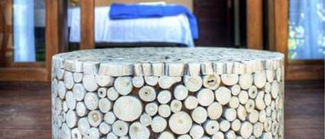 A round wooden table with a unique design made from stacked logs, placed on a wooden deck.