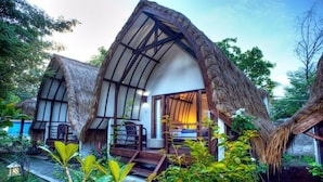 Un bungalow au toit de chaume, doté d’un escalier en bois menant à l’entrée, et entouré d’une végétation luxuriante.
