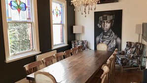 A dining area with a long wooden table, multiple chairs, a chandelier, and two stained glass windows. - 94 Highett - Luxury 5 bedroom, 3 bathroom, 3 car park House in the Inner City (Richmond)