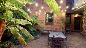 An outdoor patio with a brick floor, a table with chairs, and string lights. - 94 Highett - Luxury 5 bedroom, 3 bathroom, 3 car park House in the Inner City (Richmond)