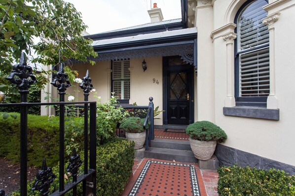 A house with a black door, white walls, and a small front garden with potted plants.