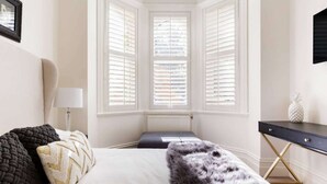 A bedroom with a bed, a nightstand, a lamp, a dresser, and a window with shutters. - 94 Highett - Luxury 5 bedroom, 3 bathroom, 3 car park House in the Inner City (Richmond)