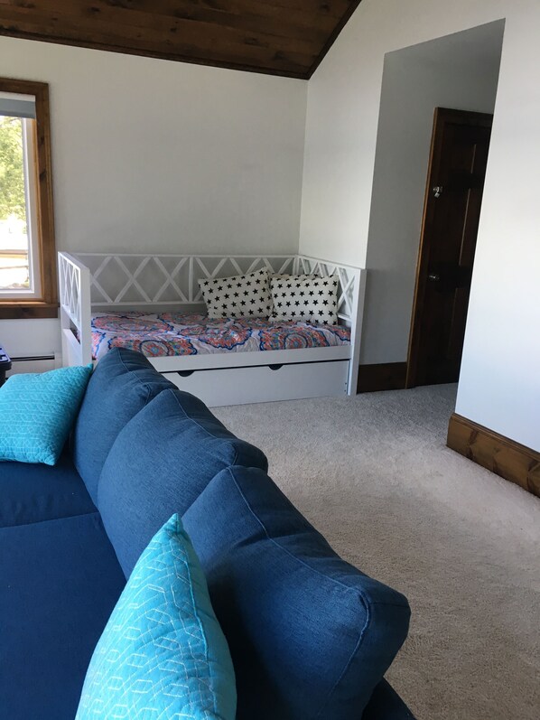 A bedroom with a bunk bed, a blue sofa with patterned cushions, and a window with a view of greenery. - Modern 300 ft lakefront with pool (Mayville)
