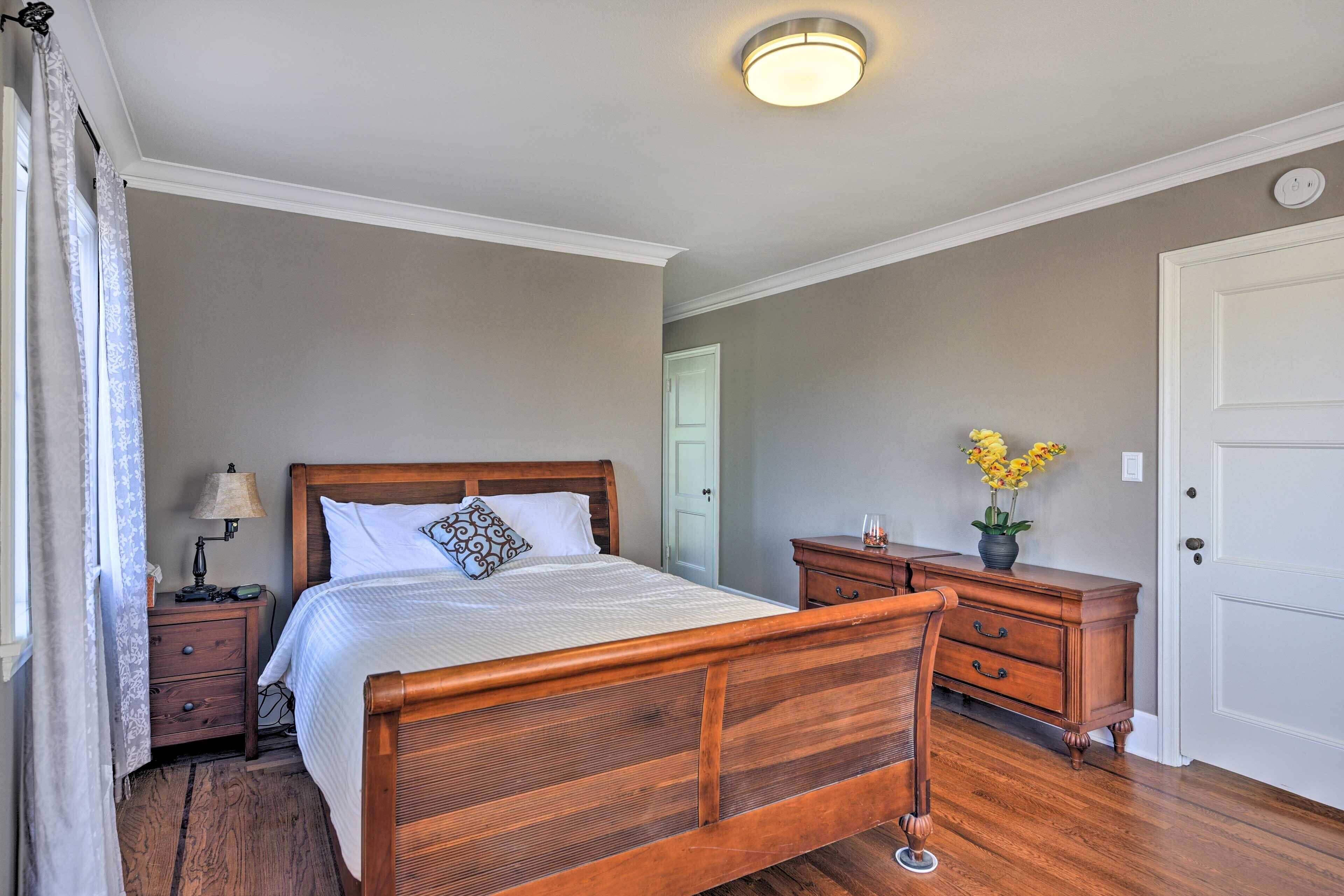 A bedroom with a wooden bed, a nightstand, a dresser, a lamp, and a vase with flowers.