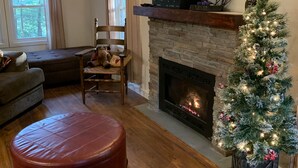 Un salon chaleureux avec une cheminée, un téléviseur, un sapin de Noël et un coin salon confortable.