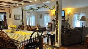 Un salon chaleureux avec une cheminée, un coin repas avec une nappe à carreaux et un sapin de Noël.