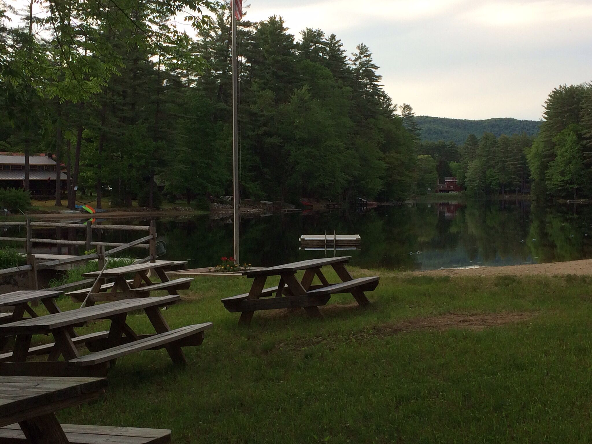 Des tables de pique-nique au bord d’un lac, avec une clôture en bois et des arbres en arrière-plan.