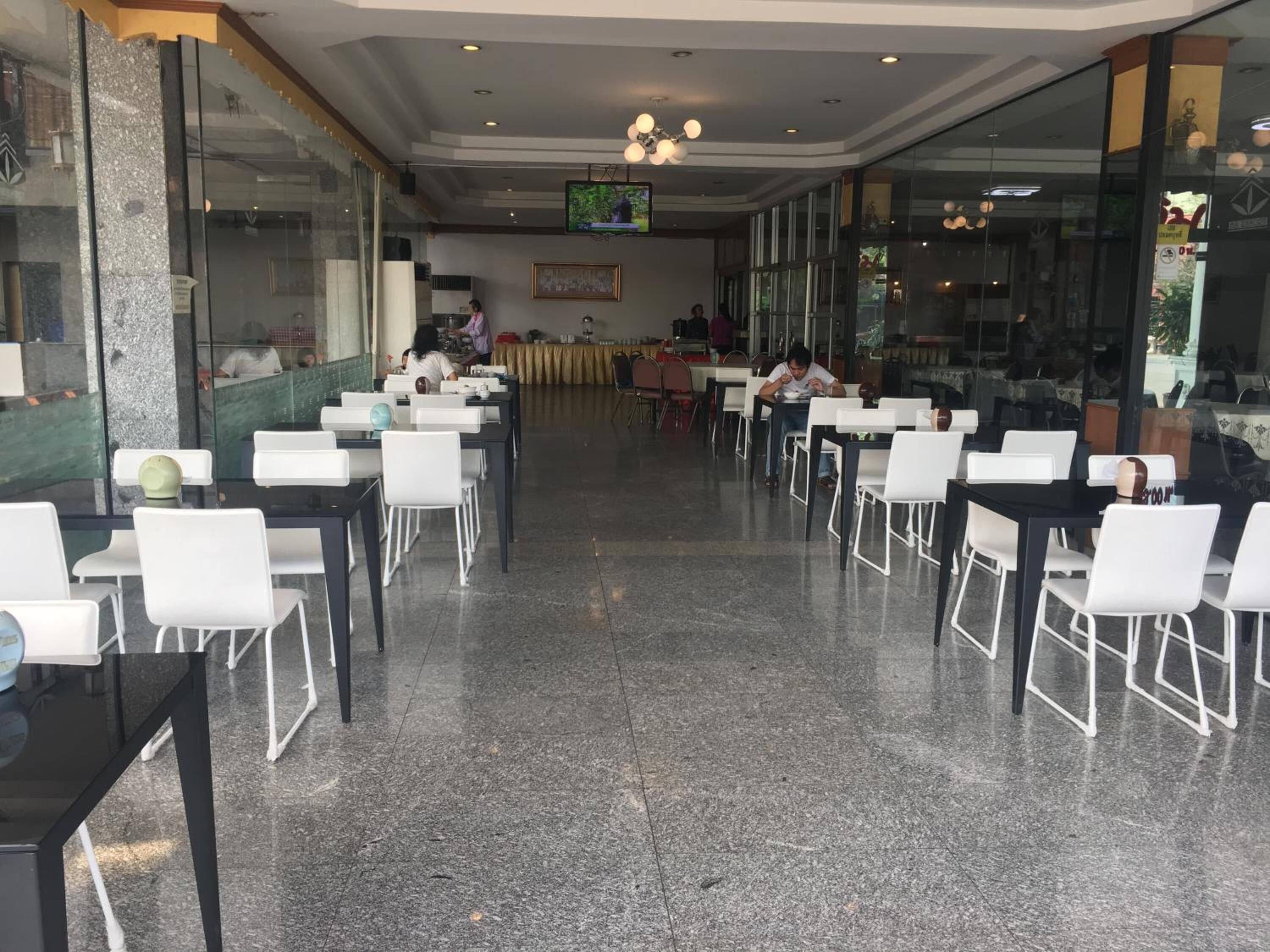 Un vaste espace de restauration intérieur, doté de nombreuses tables et chaises, d’un téléviseur fixé au mur et d’un design de plafond moderne.