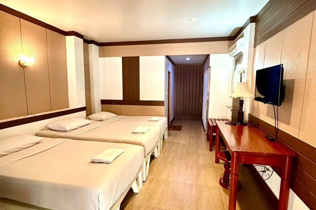 Quarto de hotel com duas camas de solteiro, uma mesa de madeira, televisão e corredor que dá para outro quarto.