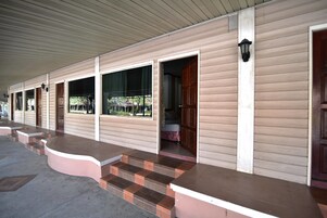 Filas de habitaciones de motel con entradas individuales, un corredor cubierto y un pequeño espacio exterior con escalones que conducen a la entrada.