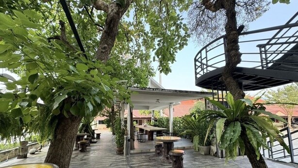 An outdoor patio area with wooden tables and benches, surrounded by trees and potted plants. - Bansuan Resort (Nakhon Sawan)