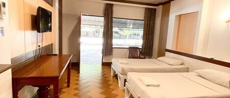 A hotel room with a wooden floor, a bed, a small table, and a TV mounted on the wall.