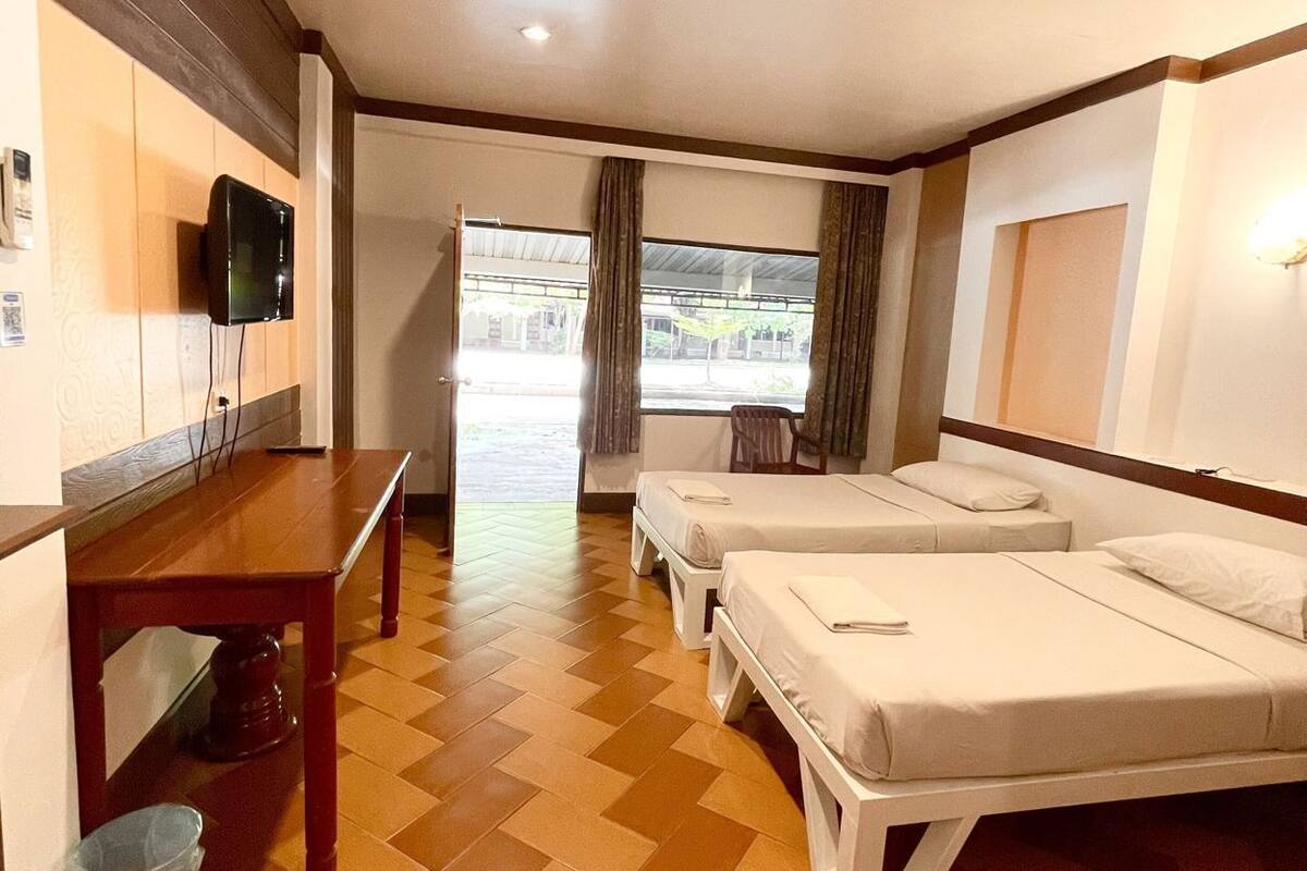 Quarto de hotel com piso de madeira, televisão fixada na parede, uma mesa e duas camas.