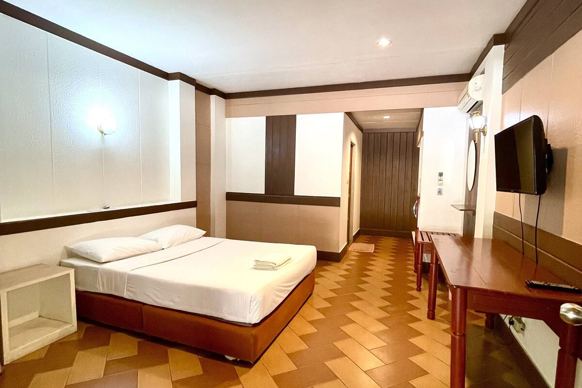 Quarto de hotel com cama, escrivaninha, cadeira, televisão e banheiro.