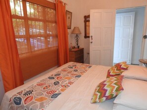 Une chambre à coucher avec un lit, des rideaux orange, une lampe, une porte et une petite table.