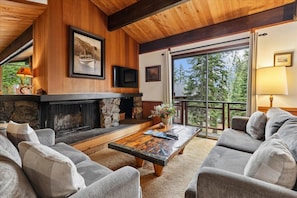 A cozy living room with a fireplace, comfortable seating, and a large window offering a view of the outdoors.