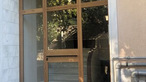 A building entrance with a wooden door and a glass panel, a number '12' sign, and a metal handrail.