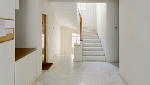 A spacious, well-lit hallway with a wooden staircase leading to an upper floor.