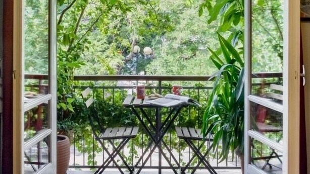 An open balcony with a table and chairs, surrounded by lush greenery and trees.