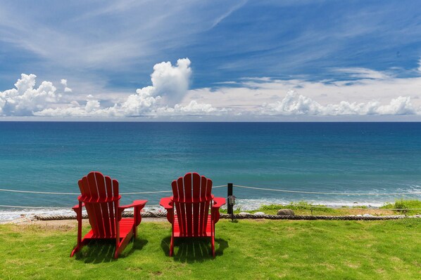 Two red Adirondack chairs facing a view of the ocean with a rope barrier and a grassy area. - Guesthouse high Wave (Shoufeng)