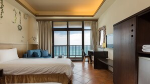 Ein Hotelzimmer mit zwei Betten, einem Schreibtisch, einem Sessel, einem Fernseher und einem Balkon mit Meerblick.