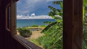 Blick aus einem Fenster auf einen Strand mit blauem Himmel und Wolken.