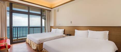 A hotel room with two beds, a red chair, a large window with a view of the sea, and a wooden headboard.
