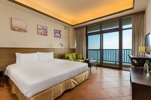 A hotel room with a large bed, a green sofa, a desk with a lamp, and a view of the sea through large windows. - Guesthouse high Wave (Shoufeng)