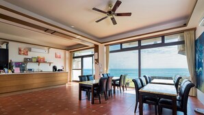 Ein geräumiges Zimmer mit einem großen Esstisch und Stühlen, einem Deckenventilator und Blick aufs Meer.