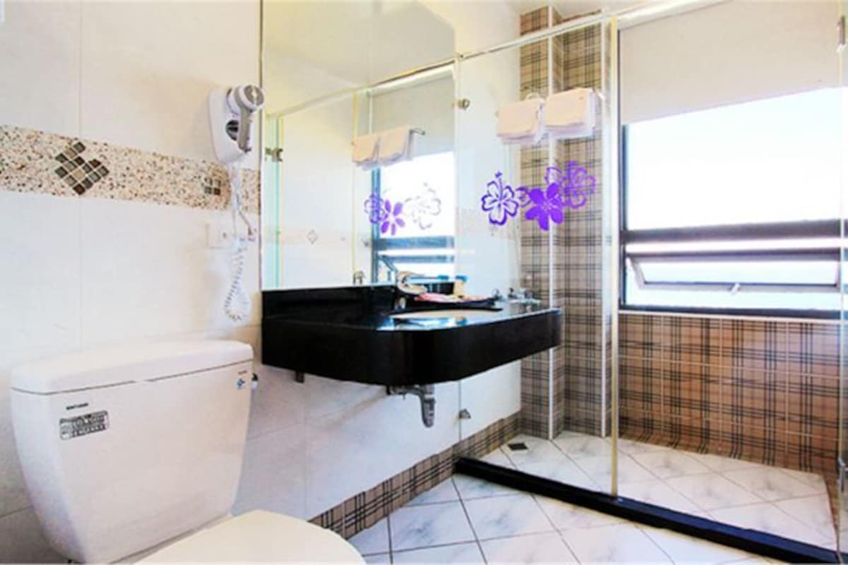 A bathroom with a white toilet, a black sink, a mirror, and a shower area.