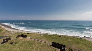 Blick auf die Küste mit felsigem Ufer, einer Wiese mit Holzgebäuden und dem Meer im Hintergrund.