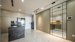 A modern kitchen with a marble island, a built-in oven, and a sliding glass door leading to a dining area. - Wow! Homes by Christine - Vinhomes Luxury (Ho Chi Minh City)