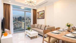 A modern living room with a sofa, dining table, and a large window offering a city view. - Wow! Homes by Christine - Vinhomes Luxury (Ho Chi Minh City)