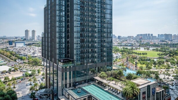 A high-rise building with a modern glass facade, surrounded by a landscaped area with a pool and palm trees. - Wow! Homes by Christine - Vinhomes Luxury (Ho Chi Minh City)